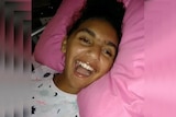Head and shoulders shot of Denishar Woods laughing with head on pink pillow