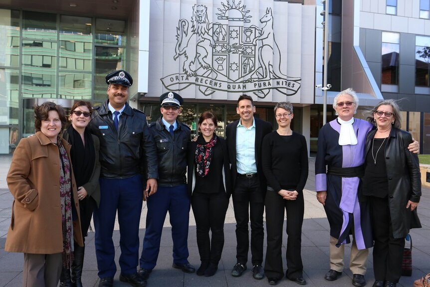 A group of people including police, lawyers and a judge stand outside a court room