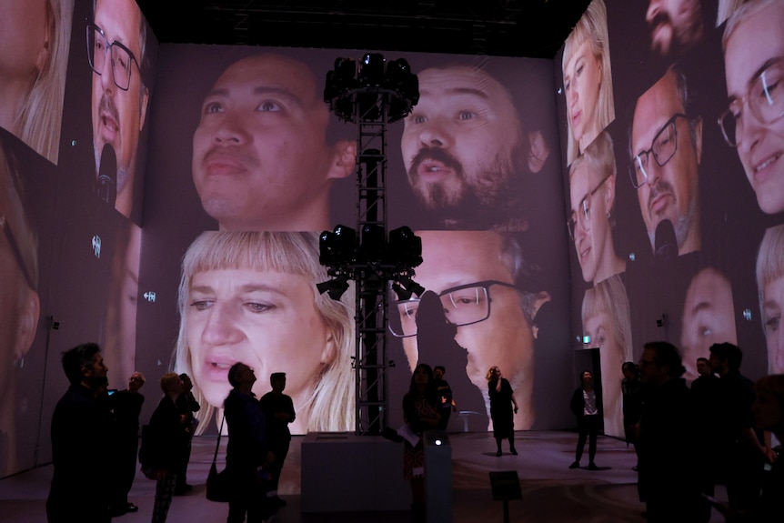 A large room with wall-to-wall projections of people's faces, recorded and tracked using surveillance.