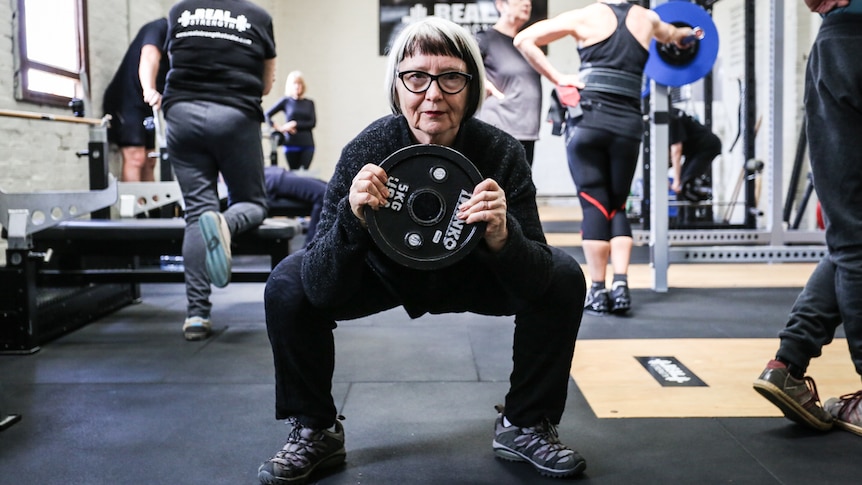 Roz Avent squatting while holding a five kilogram weight.