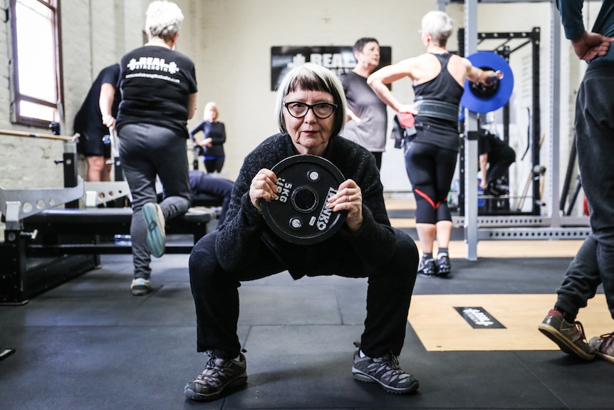Roz Avent squatting while holding a five kilogram weight.