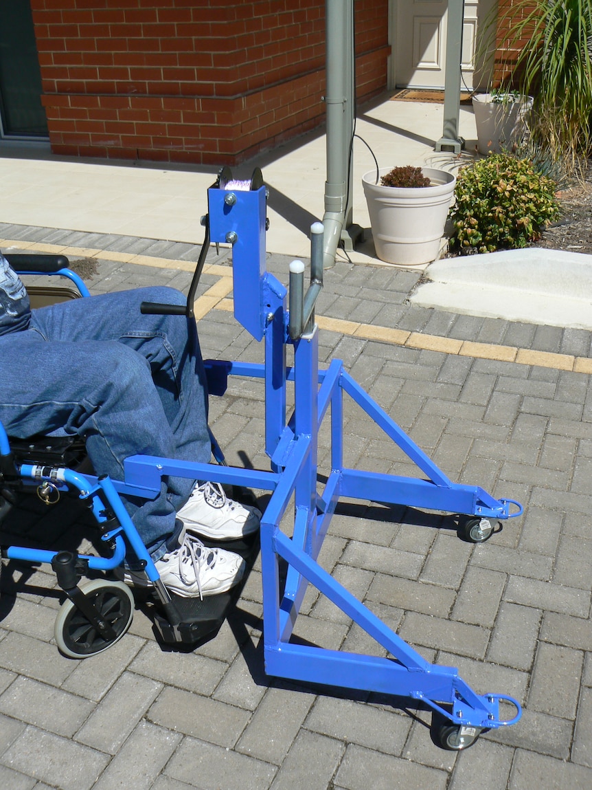 A man sits in a wheelchair with a blue bindozer attached to the front