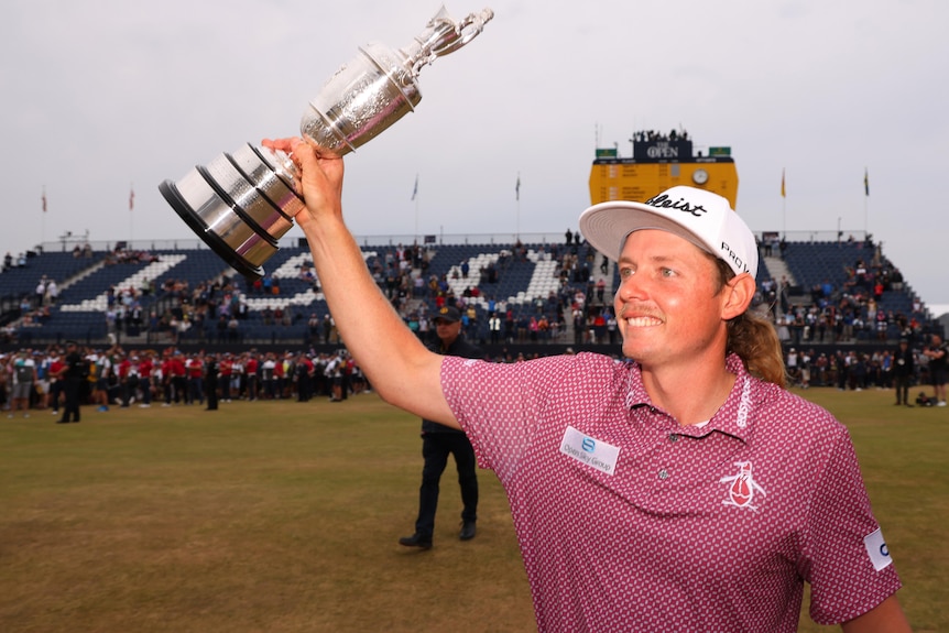 Cameron Smith smiles while holding up the Claret Jug in one hand