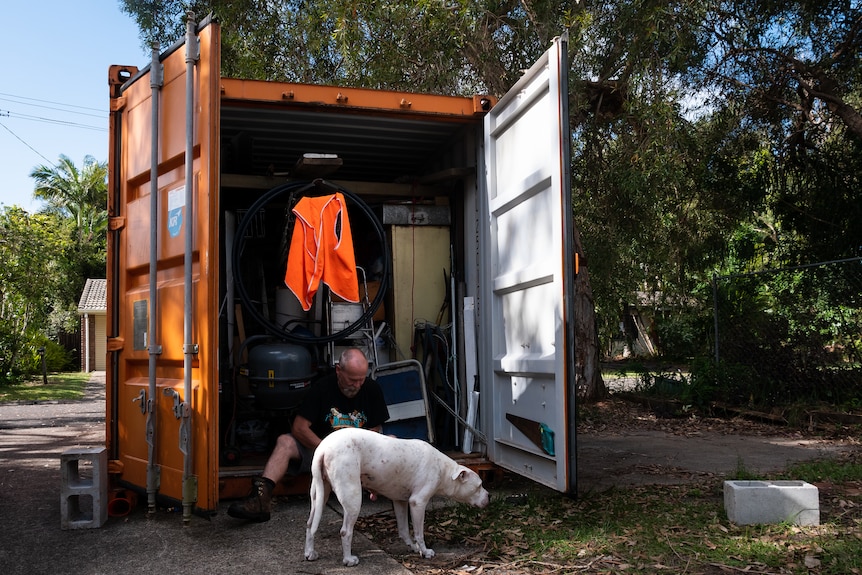 man sits at bottom of shipping container with dog