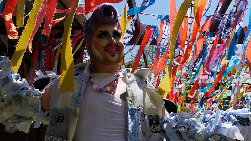 a drag performer stands under colourful streamers