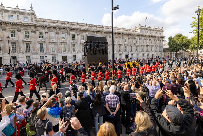 Crowds of people watch on as the Queen's coffin passes in a procession on the street. 