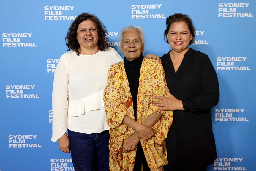 Three women stand smiling with blue SFF-branded wall behind them. Freda Glynn, eldest, in middle.