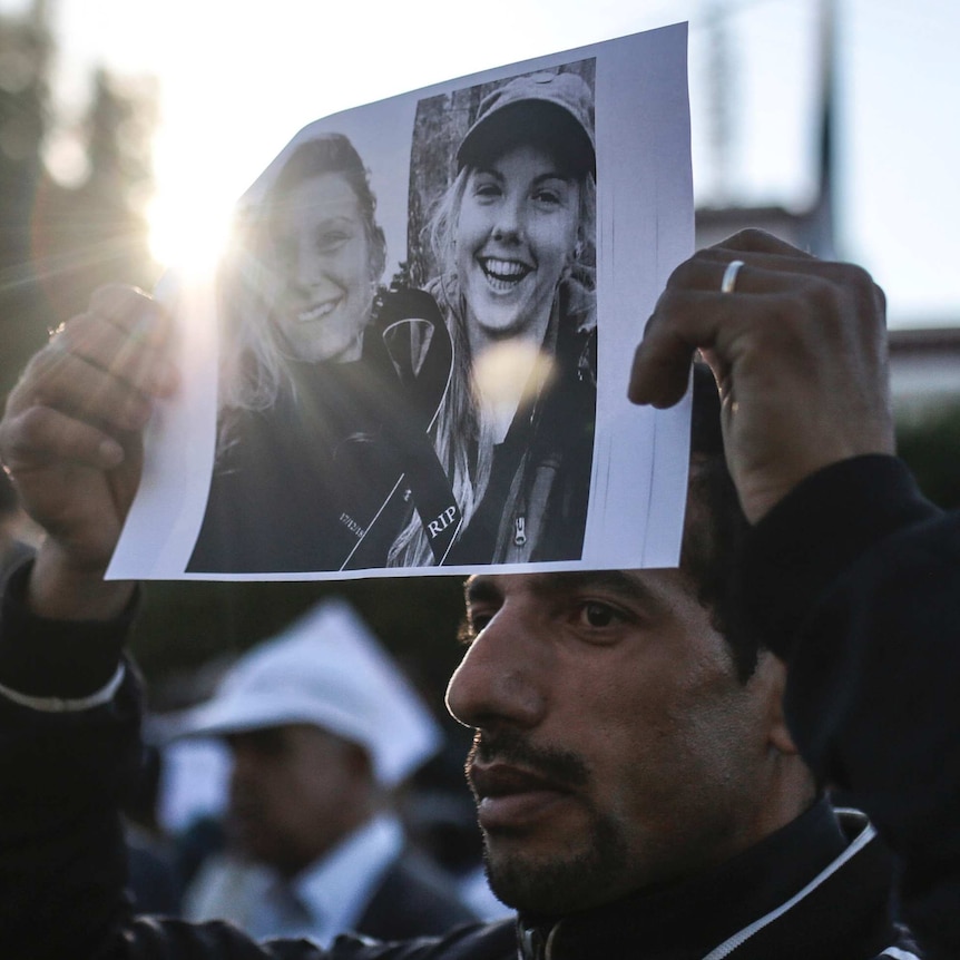 a man holds a piece of paper showing two terror victims above his head