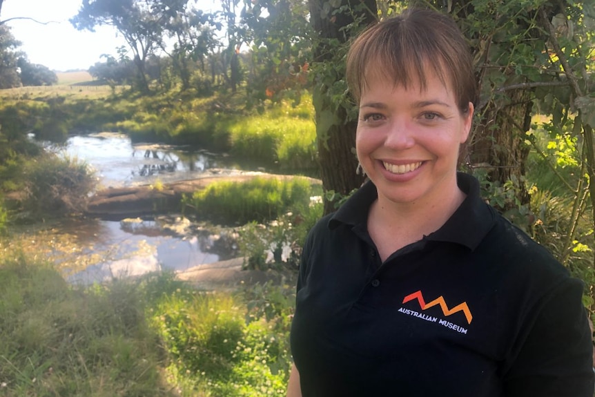 A woman smiles, standing in front of a pond.