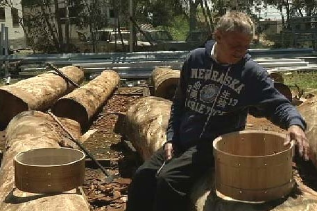 Chris Brady sitting on a sawn log with drum barrels.