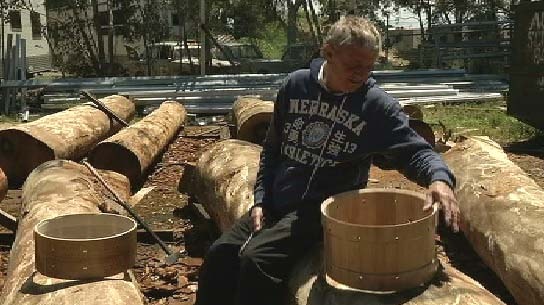 Chris Brady sitting on a sawn log with drum barrels.