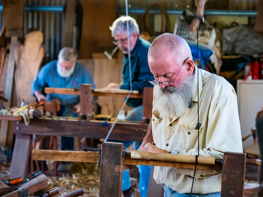 Three woodworkers using pole lathes in a workshop.