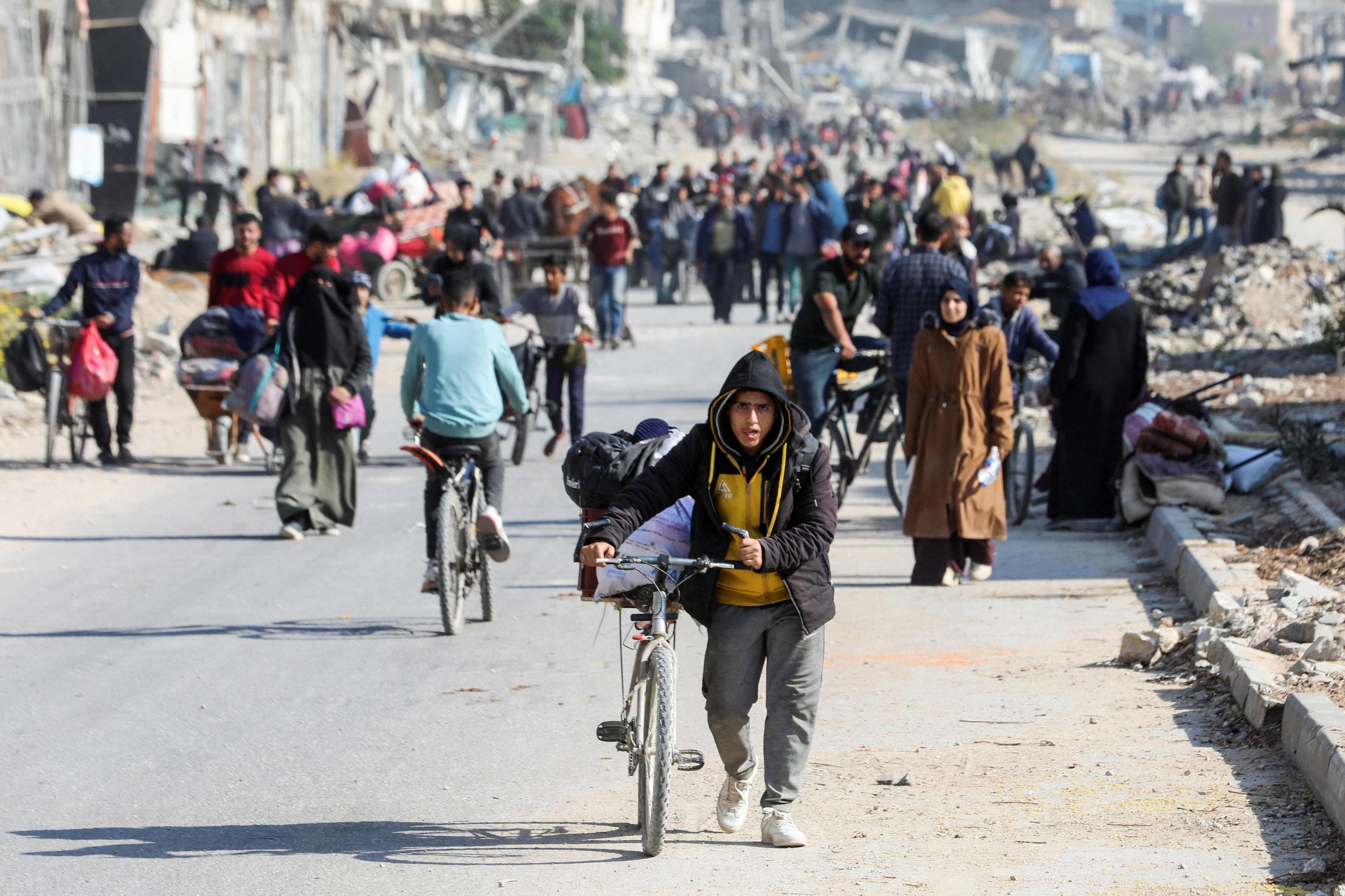 A group of Palestinian people walking down a heavily bombed and destroyed road