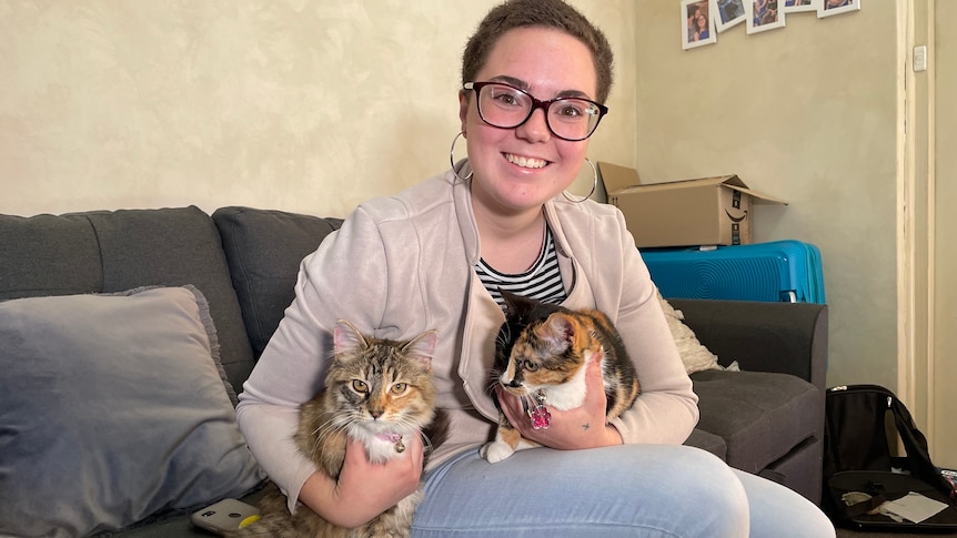 A woman with two cats sitting on a sofa