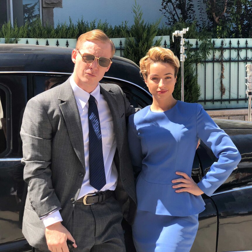 A man in a suit and sunglasses poses with a woman