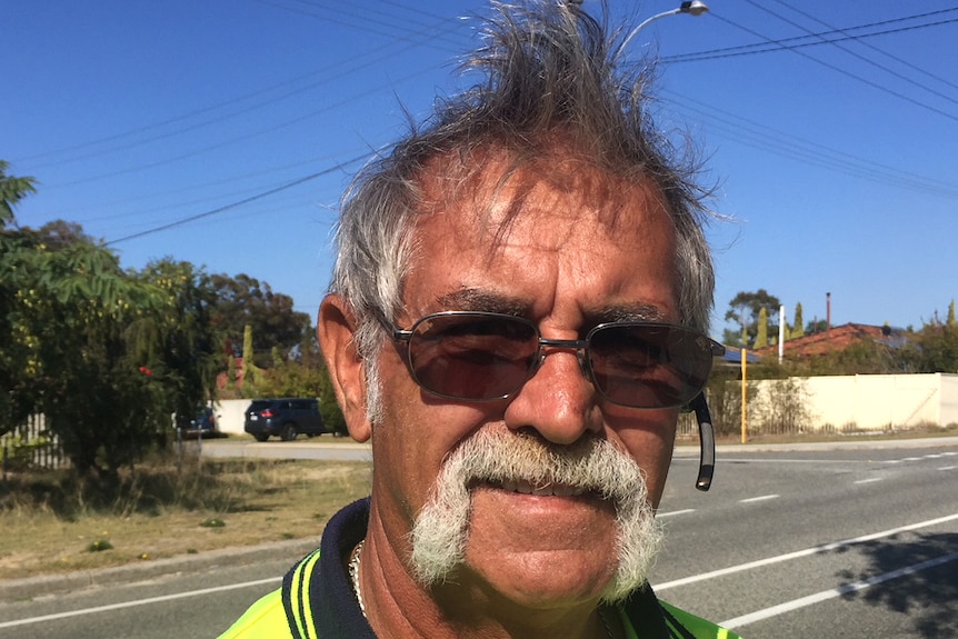 Thornlie resident Dirk Jagers in a yellow fluro top stands on the street, with powerlines and sky in the background.