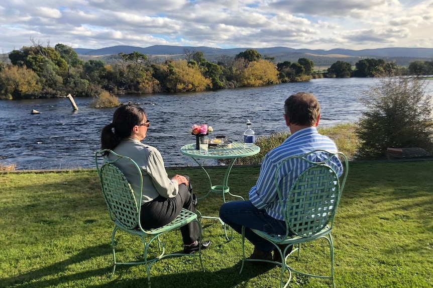 Ross and Mary Mace sit outside watching the river while drinking their homemade gin at  Lawrenny Estate, Tasmania.