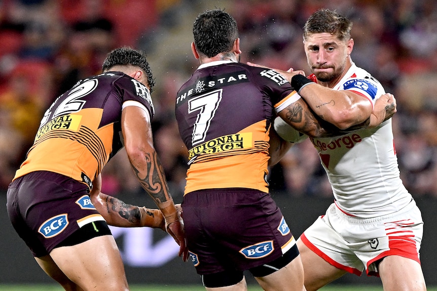 A St George Illawarra NRL player holds the ball as he is met by two Brisbane Broncos defenders.