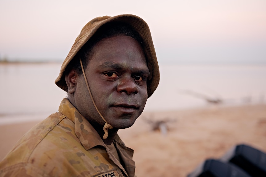 an aboriginal man in army uniform looking directly at the camera on a beach