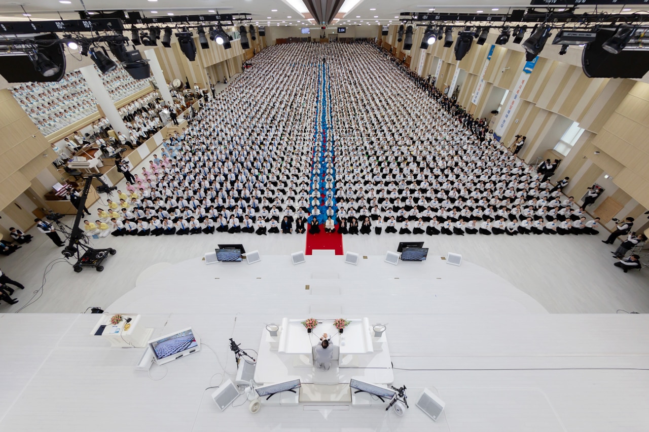 Un salón lleno de cientos de personas con pantalones negros y camisas blancas. 