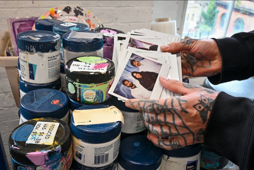 Two hands hold a stack of polaroids, they lean against paint containers.