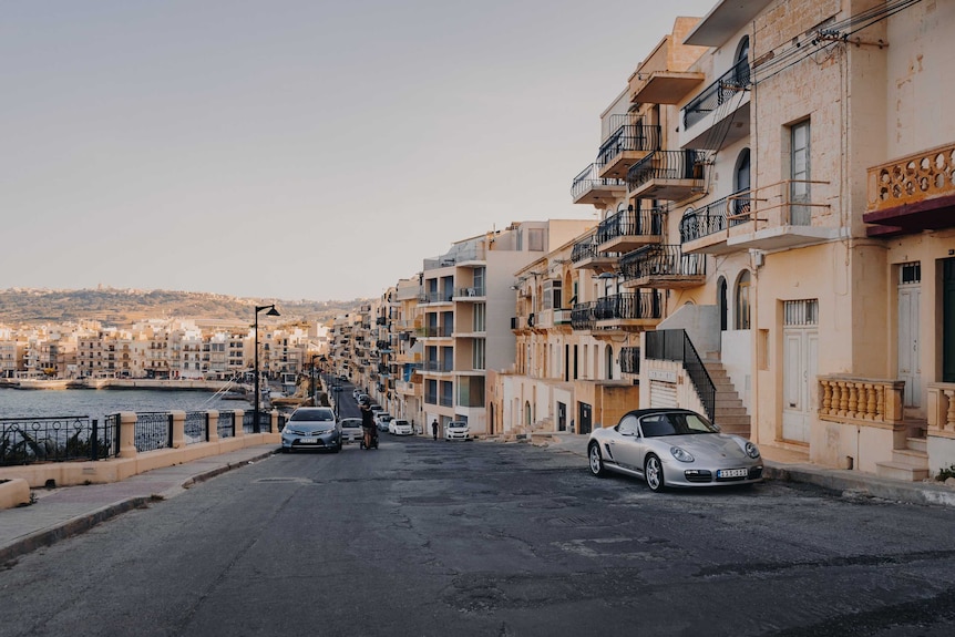 A street along the coast in Malta at sunset, with cars in the foreground.