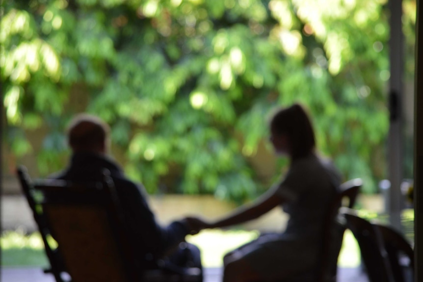 An out of focus shot of an elderly man holding a young girl's hand on a deck outside.