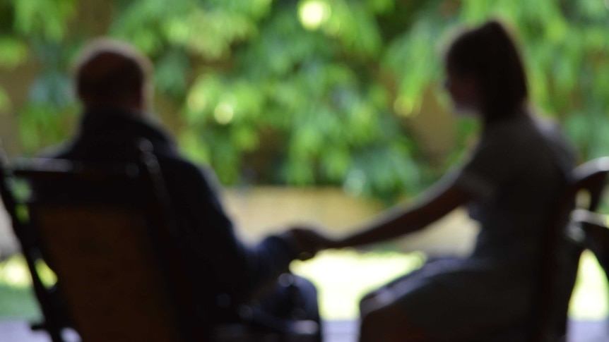 An out-of-focus shot of an elderly man holding a young girl's hand on a deck outside.