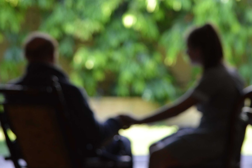 An out of focus shot of an elderly man holding a young girl's hand on a deck outside.