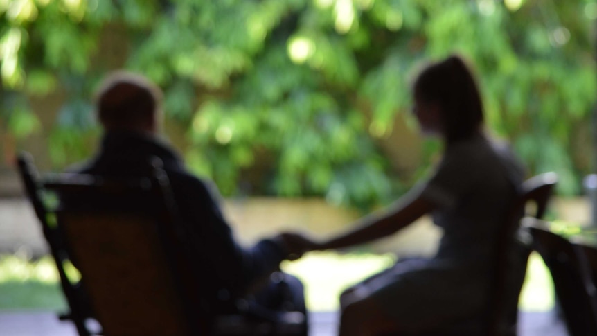 An out of focus shot of an elderly man holding a young girl's hand on a deck outside.