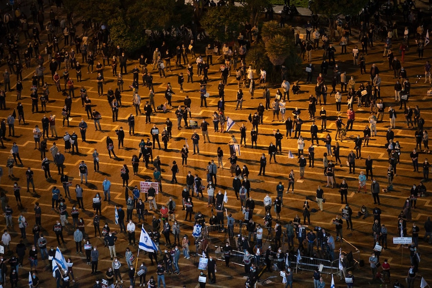 An aerial photo of dozens of people standing metres apart at a night protest