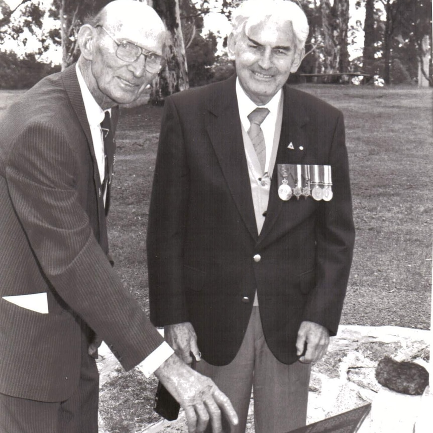 A black and white picture of two men standing at a memorial.