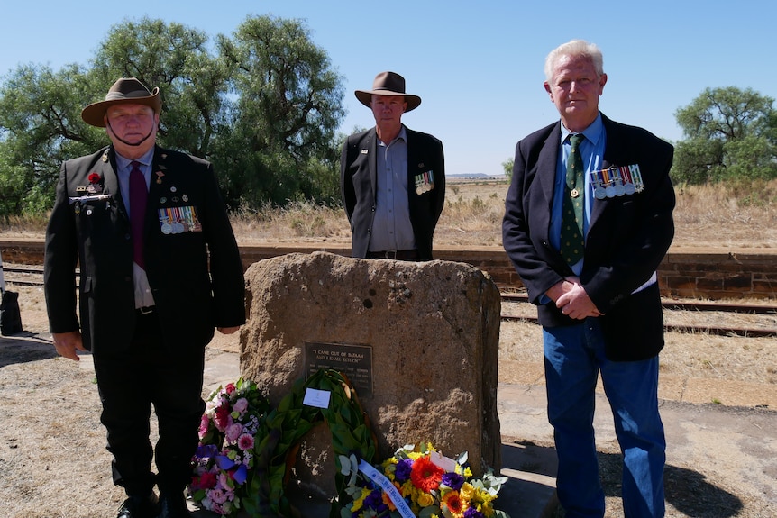 three men in uniform by a military memorial