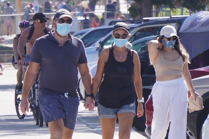 People wearing face masks walk along a footpath at Cottesloe Beach.