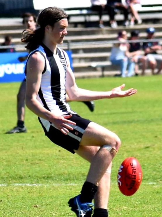 A young male wearing black and white football guernsey kicking a red football