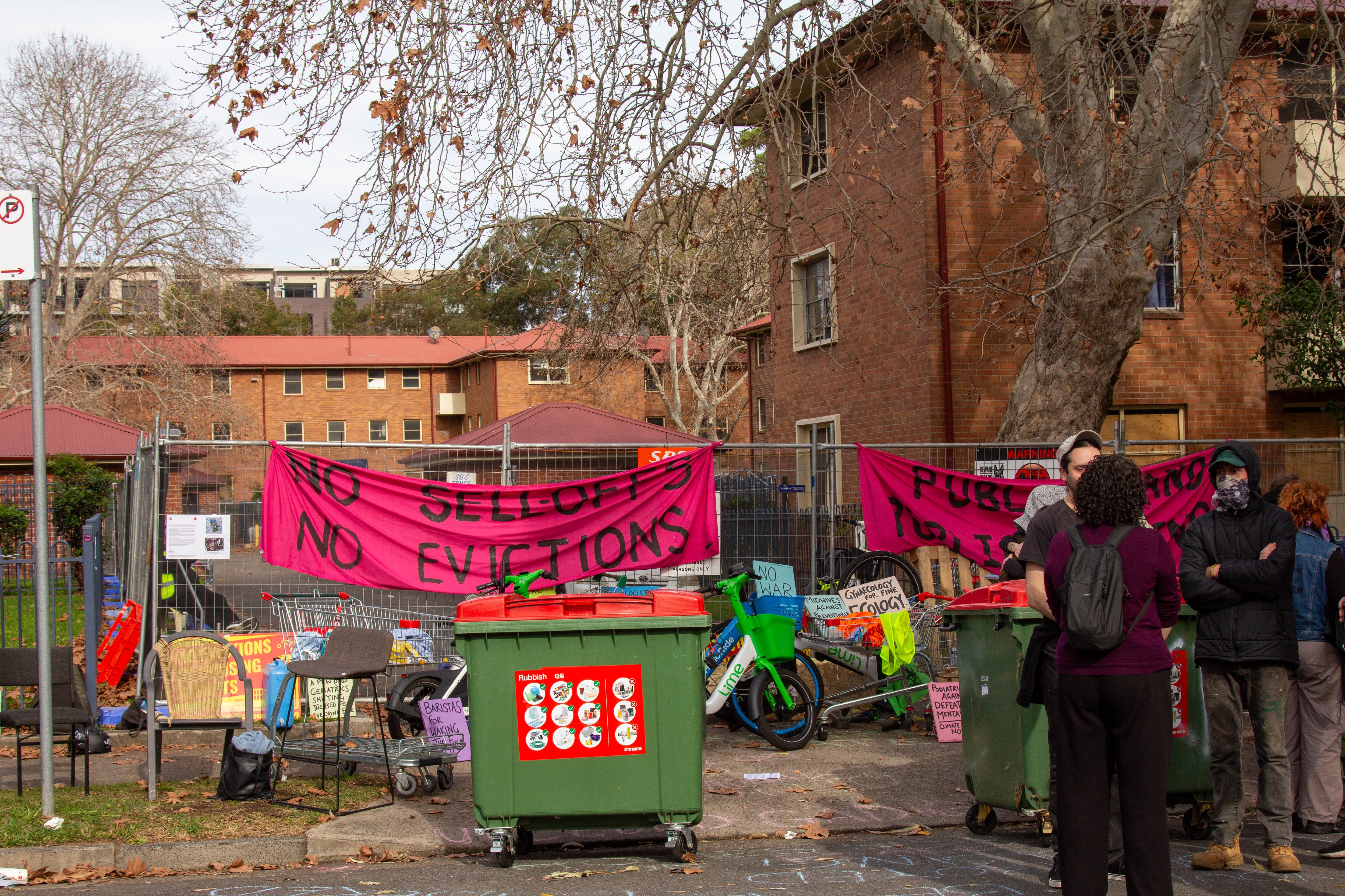 A blockade of e-bikes, protest banners and bins block access to a laneway.