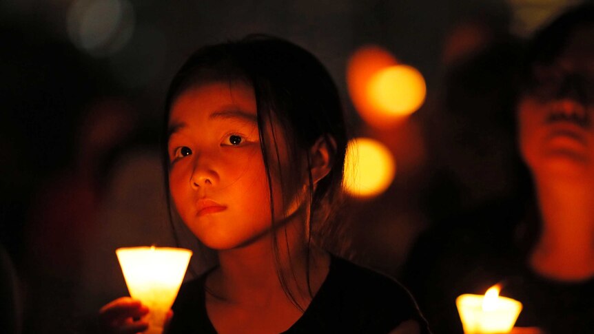 A young girl holds a candle around others at night during a vigil in Hong Kong.