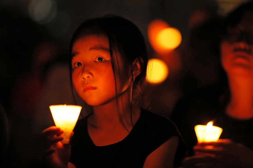 A young girl holds a candle around others at night during a vigil in Hong Kong.