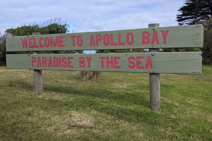 A wodden sign with red writing that says Welcome to Apollo Bay, paradise by the sea