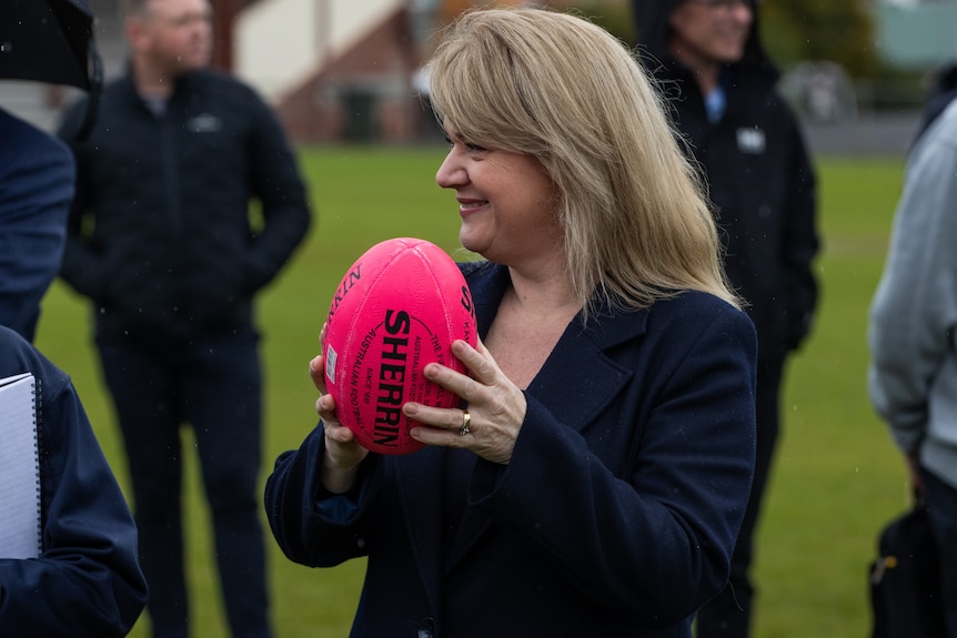 A woman with blonde hair holds pink football and smiles