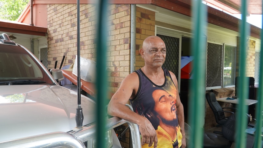 A man stands behind a fence and next to a car