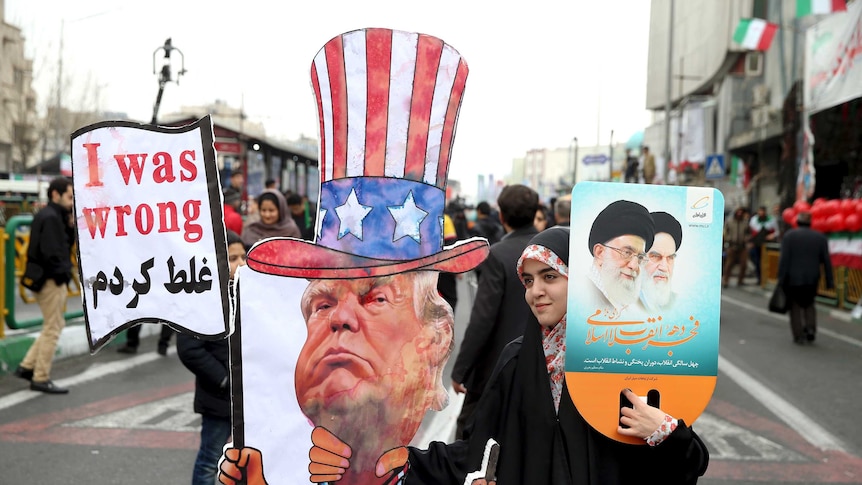 A woman holds up a caricature of Donald Trump in Uncle Sam attires holding a sign that reads 'I was wrong' in English and Arabic