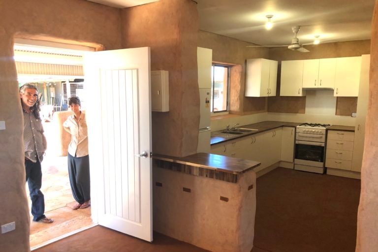 Two people stand outside new kitchen which has rendered falls