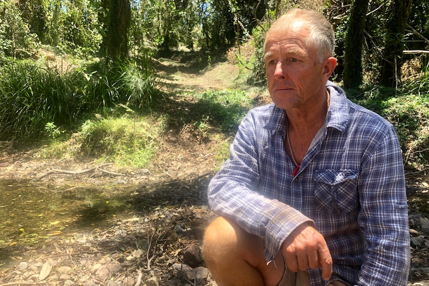 John Tidy looking worried and crouching in a creek on rocks where water usually would be flowing.