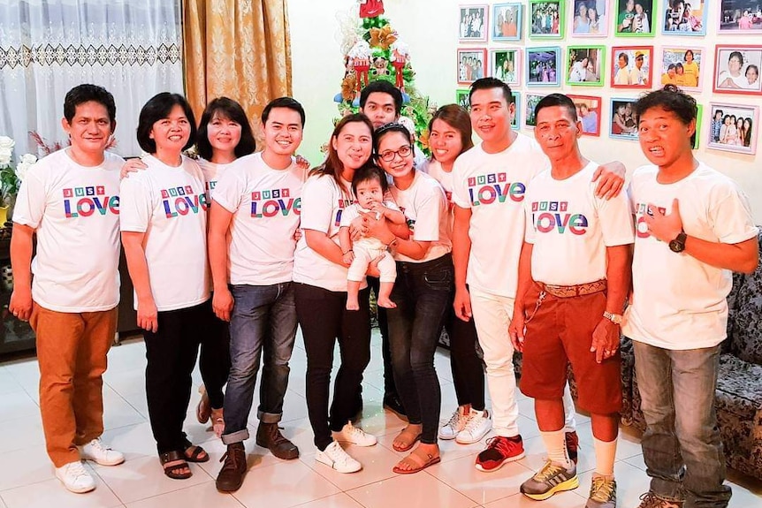 A Filipino family wearing matching t-shirts pose in front of a Christmas tree 