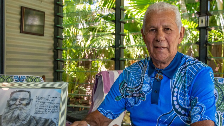 Robert Isaacs sitting with a blue shirt with Aboriginal patterns on it, with a drawing of Samuel Isaacs