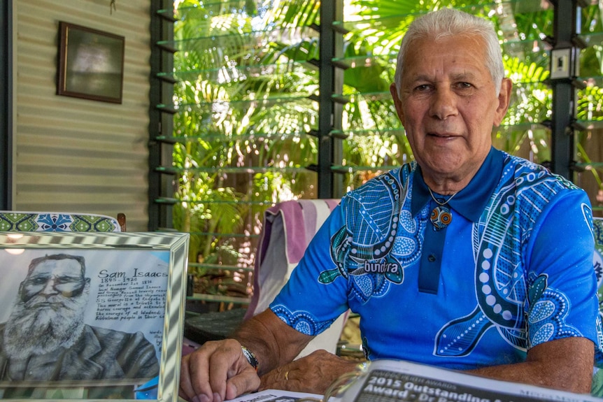Robert Isaacs sitting with a blue shirt with Aboriginal patterns on it, with a drawing of Samuel Isaacs