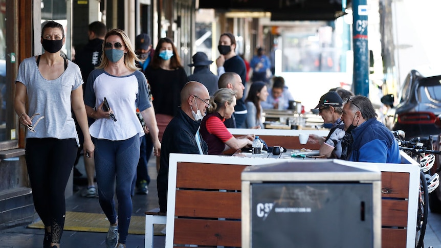 Two women in fitness clothing walk on footpath as others sit down outside restaurants on Chapel Street.