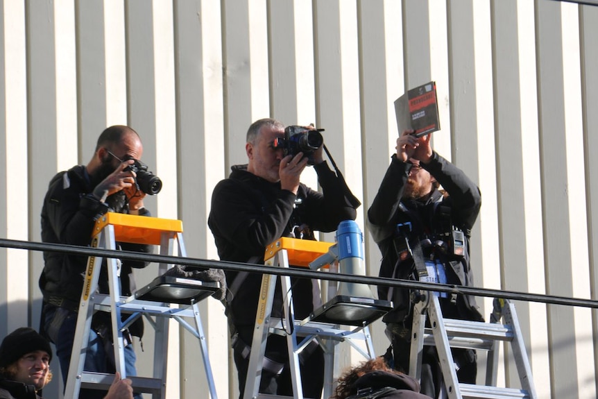 Spencer Tunick takes a photograph while standing on a ladder between two other photographers.