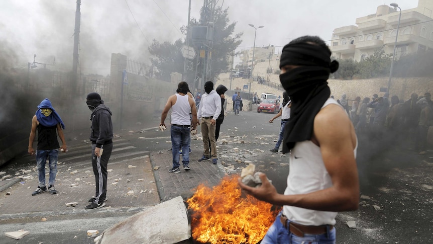 A masked Palestinian holds stones during clashes with Israeli police